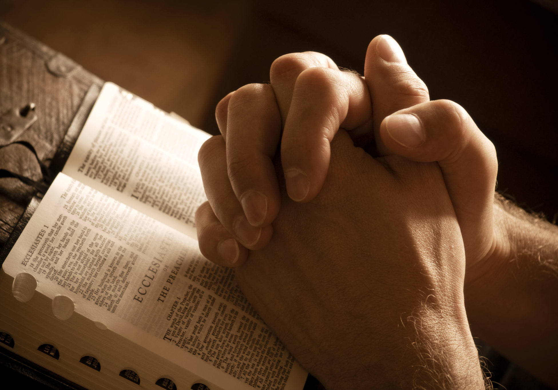 Hands closed in prayer on an open bible